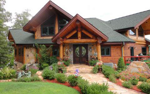 Rustic luxury log cabin home in the Georgia mountains, featuring a grand entrance, lush landscaping, and a stone pathway