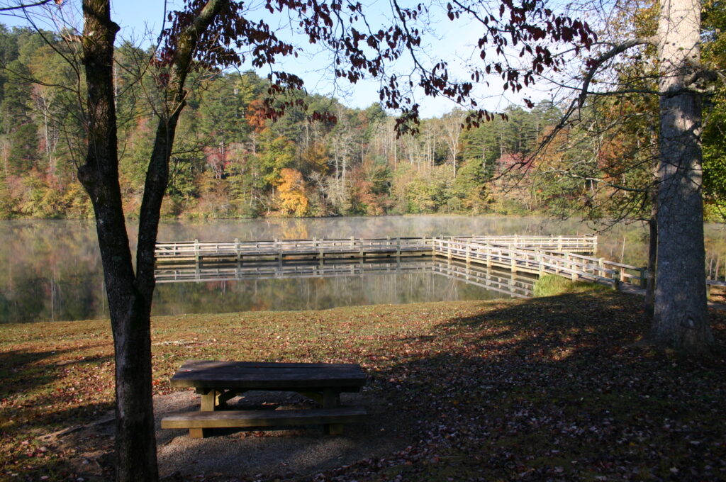 Lake with a wooden fishing pier, autumn trees, and a picnic table